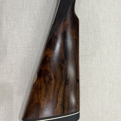 Coronha de espingarda em madeira castanha polida com base preta e faixa branca sobre tecido claro