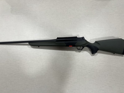 Espingarda preta e cinzenta com empunhadura texturizada encostada numa parede branca