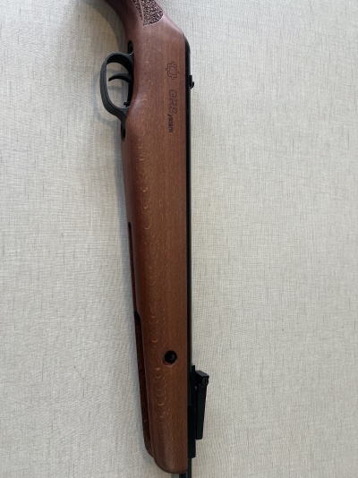 Espingarda com coronha em madeira castanha e corpo preto sobre fundo cinza