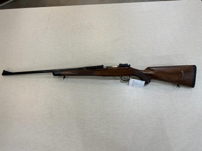 Rifle de coronha em madeira escura com cano longo sobre superfície clara