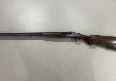 Espingarda de canos duplos com coronha em madeira castanha sobre fundo cinza.