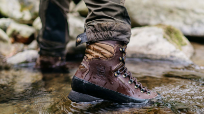Bota de caminhada castanha molhada em água rasa junto a pedras.