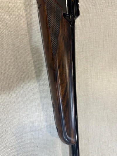Coronha de espingarda em madeira escura com textura quadriculada e parte metálica preta