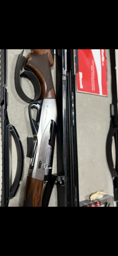 Espingarda de caça com coronha em madeira castanha e partes metálicas prateadas numa caixa acolchoada.