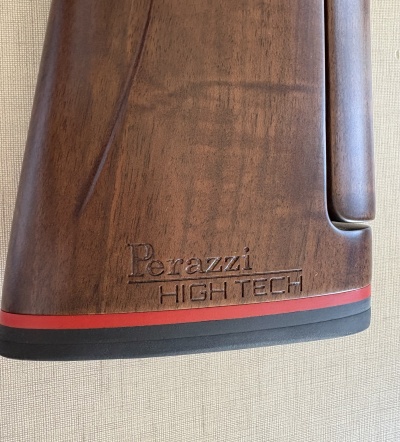 Peça de madeira castanha com gravação Perazzi HIGH TECH e faixa preta e vermelha