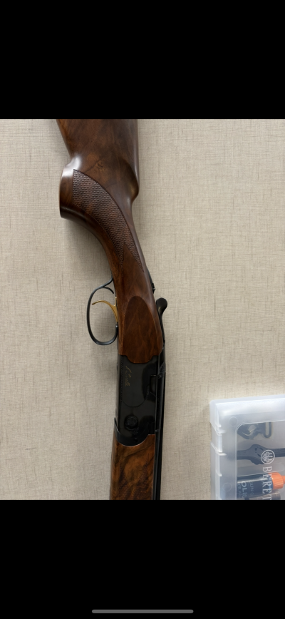 Espingarda de caça em madeira castanha com gatilho dourado e caixa de plástico BERETTA ao lado