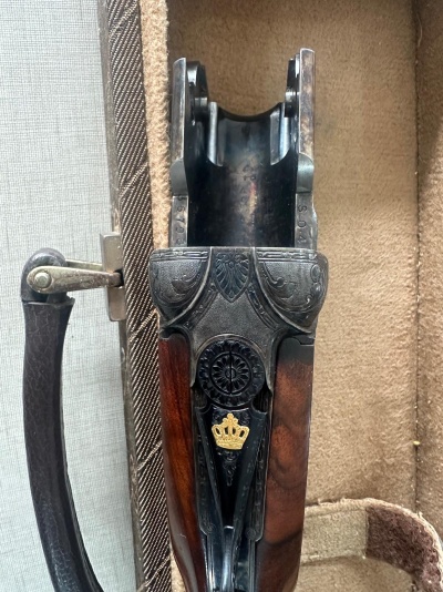 Parte superior de arma de fogo com detalhes metálicos e símbolo de coroa dourada