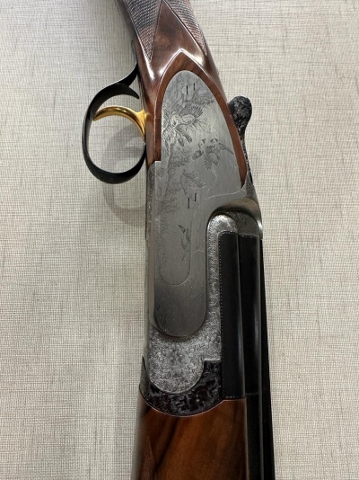 Espingarda com cabo em madeira castanha, gatilho dourado e placa lateral com gravação floral em metal cinzento