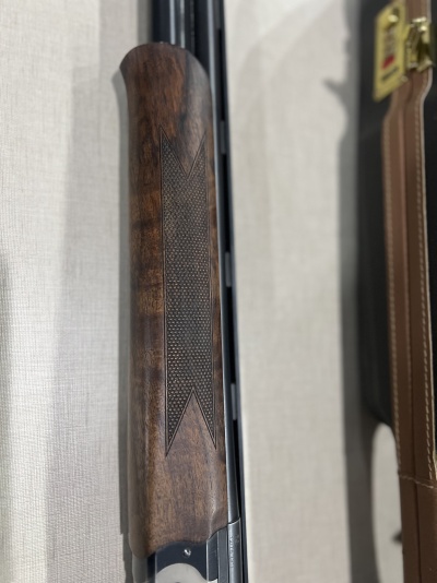 Corpo de espingarda com punho de madeira castanha texturizada e mala preta ao lado