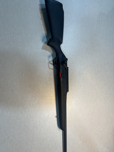 Espingarda preta com detalhe vermelho encostada numa parede clara