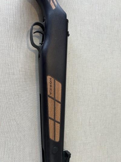 Espingarda preta com detalhes em madeira castanha e texto NORICA