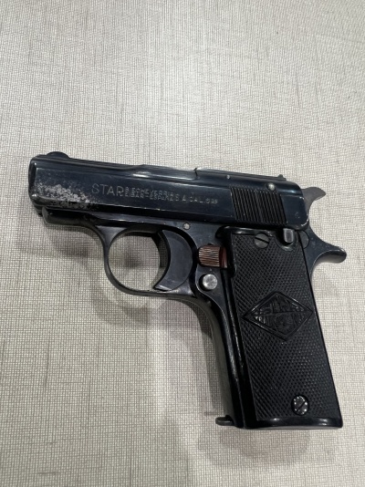 Pistola Star preta com cabo texturizado sobre superfície cinzenta