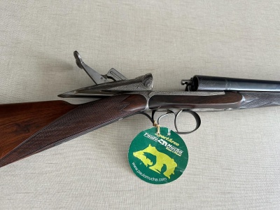 Espingarda dupla com coronha em madeira e canos metálicos, etiqueta verde pendurada