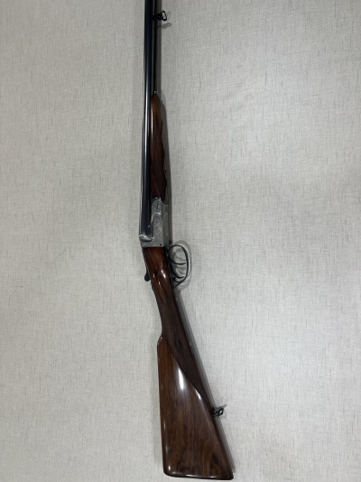 Caçadeira de madeira e metal encostada numa parede clara