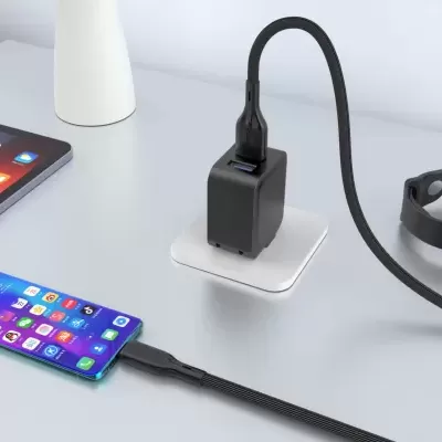Carregador USB preto com cabo ligado a dispositivos eletrónicos num fundo branco