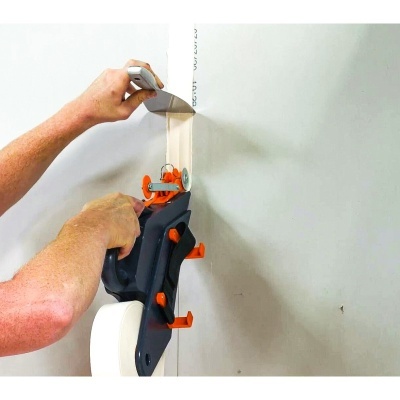 Pessoa a aplicar fita adesiva branca numa parede com aplicador preto e laranja