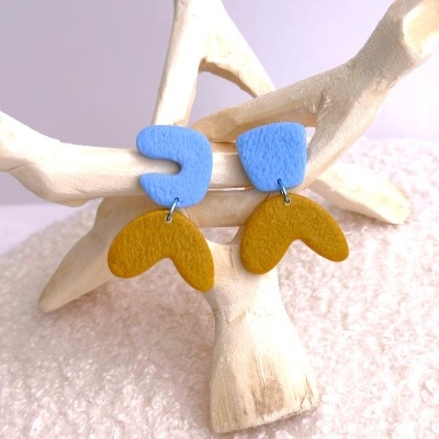 Brincos azuis e mostarda com design abstrato sobre suporte de madeira clara