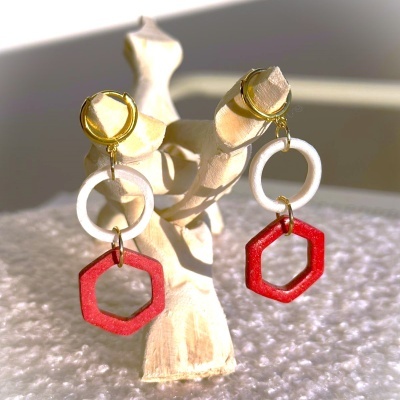 Brincos com argola dourada, círculo branco e hexágono vermelho em suporte de madeira