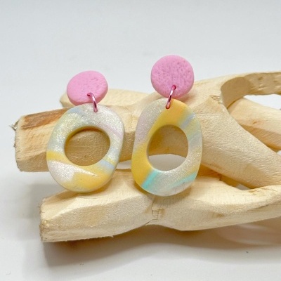 Brincos coloridos de plástico com peças ovais e circulares sobre escultura de madeira.