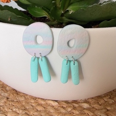 Brincos coloridos em argila polimérica sobre vaso branco e superfície de ráfia