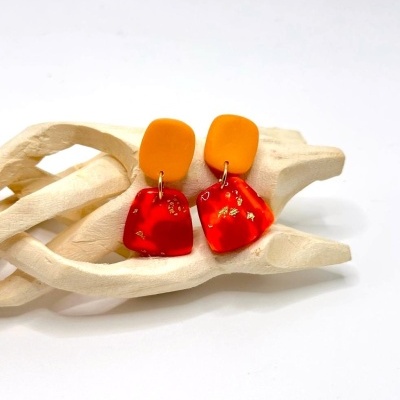 Brincos pendentes laranja e vermelho com dourado em mão de madeira
