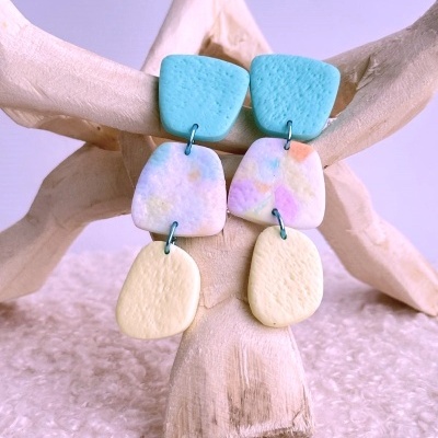 Brincos coloridos pendentes em três partes sobre suporte de madeira claro