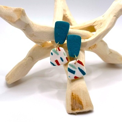 Brincos pendentes azul turquesa e branco com padrão abstrato em suporte de madeira clara