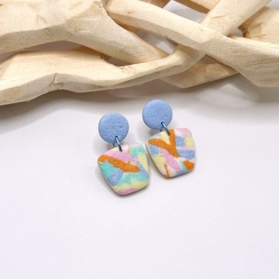 Brincos azuis com padrão pastel e fundo branco com madeira