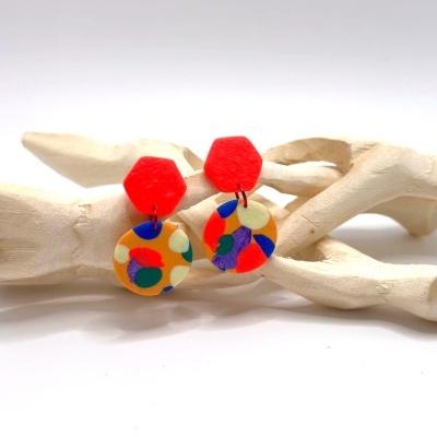 Brincos pendentes coloridos com formas geométricas e padrão multicolor sobre suporte branco