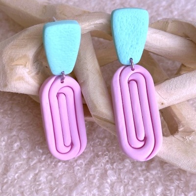 Brincos azuis e rosa sobre fundo branco felpudo com suporte de madeira