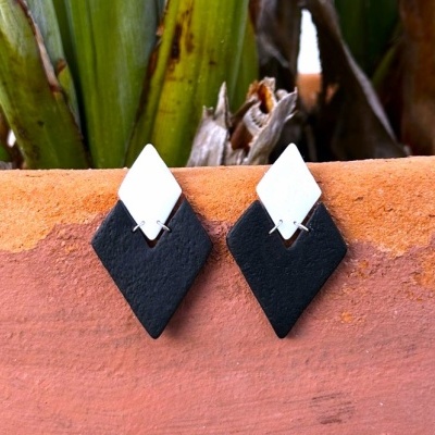 Brincos geométricos branco e preto com fundo de plantas e terracota