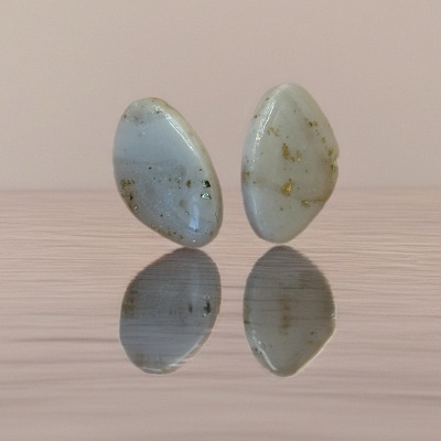 Brincos com pedras brancas e douradas refletidos numa superfície.