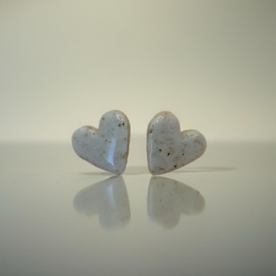 Brincos em forma de coração brancos com manchas e textura brilhante sobre superfície refletora