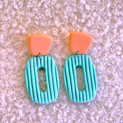 Brincos de argila cor coral e azul turquesa com textura, fundo branco felpudo
