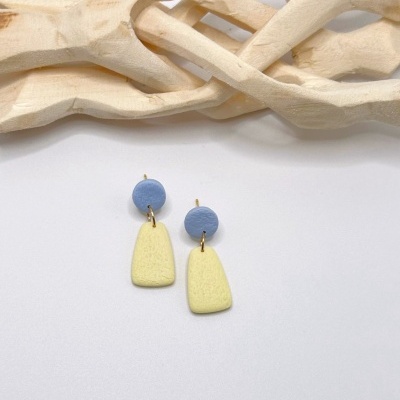 Brincos pendentes azul e amarelo sobre fundo branco com madeira clara ao fundo