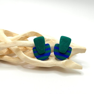 Brincos geométricos verdes e azuis sobre suporte de madeira clara