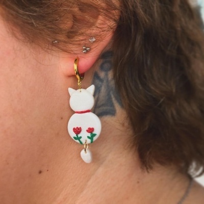 Brinco pendente dourado com pingente branco de gato e flores vermelhas