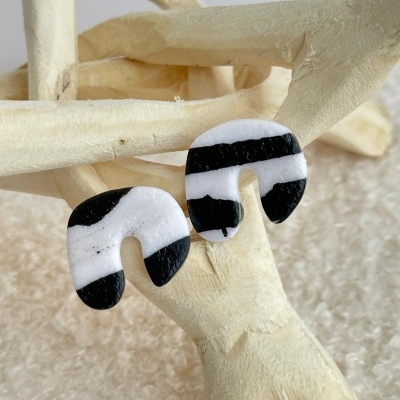 Brincos em forma de U listrados preto e branco sobre estrutura de madeira clara