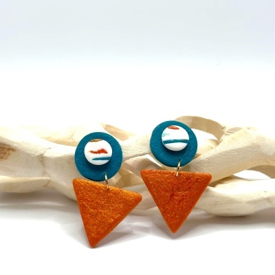 Brincos pendentes com formas geométricas em azul, branco e laranja, sobre fundo branco.