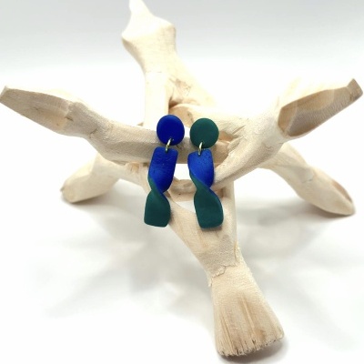 Brincos azuis e verdes pendurados em suporte de madeira clara