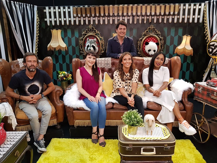 Entrevista para o programa É a vida Alvim Grupo de pessoas sentadas em sofá de couro castanho em sala decorada com máscaras e luminárias vintage