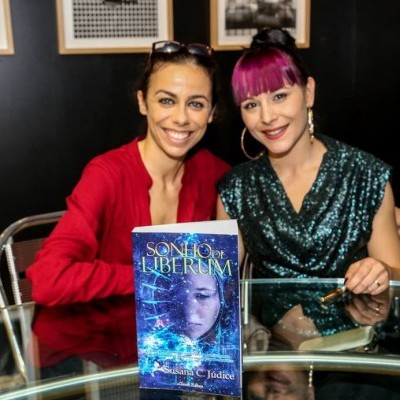 Duas mulheres sentadas atrás de uma mesa de vidro com o livro 'SONHO DE LIBERDADE' em destaque.