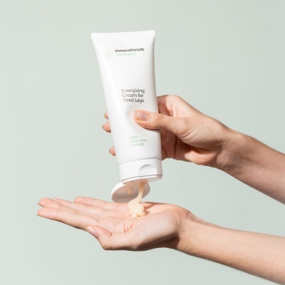 Frasco branco de creme para pernas cansadas sendo espremido na mão