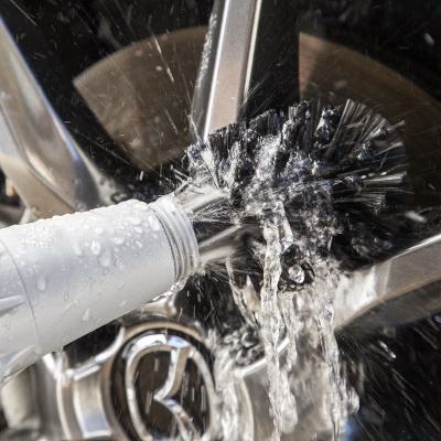 Escova preta a ser lavada com água diante de uma jante de carro Mazda