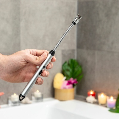 Isqueiro eléctrico prateado com tubo flexível segurado junto a uma banheira com velas ao fundo