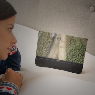 Dispositivo digital preto com colunas integradas a exibir imagem aérea de uma estrada com vegetação