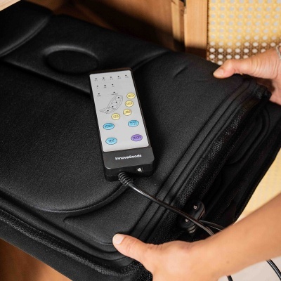 Tapete de massagem preto com controlador remoto Panasonic e mãos segurando, sobre cadeira de madeira com encosto trançado.
