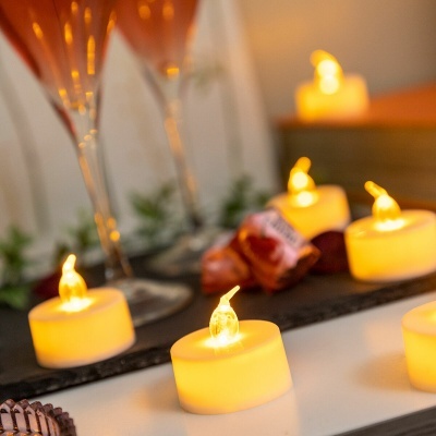 Velas LED amarelas em tealight com copos e bombons ao fundo