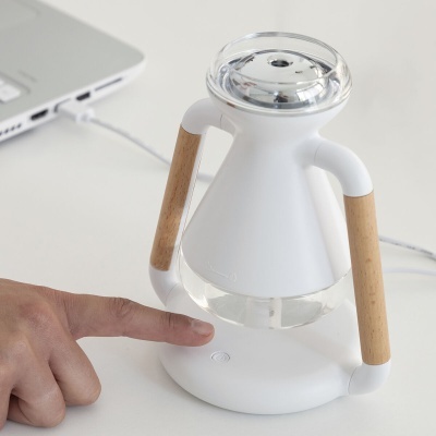 Humidificador branco com detalhes em madeira e base redonda ao lado de portátil