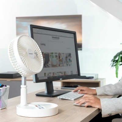 Ventoinha portátil branca numa secretária junto a monitor de computador e mãos a usar teclado e rato